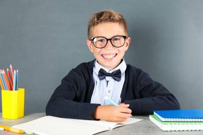 Boy in school uniform sitting at the table against board background