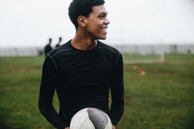Smiling soccer player standing on field holding a football looking away