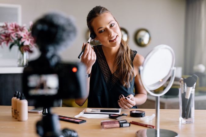 Beautiful woman using makeup brush while recording video