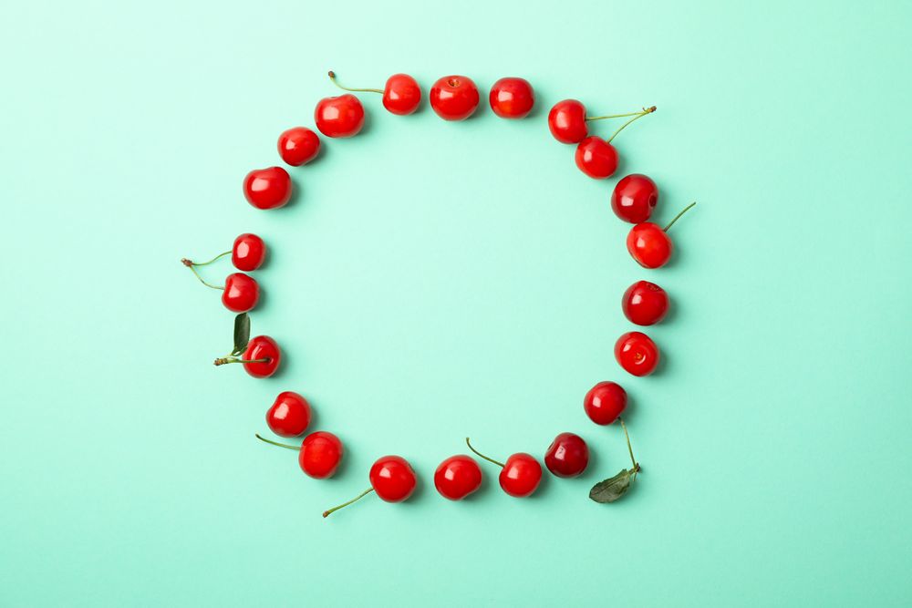 Circle made of red cherry on mint background, top view