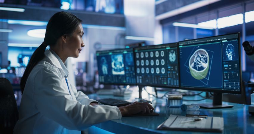 Female Asian Neuroscientist Using Desktop Computer With Human Brain CT Scans In Modern Medical Research Center Laboratory.
