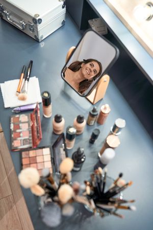 Positive woman reflecting in mirror near cosmetic products