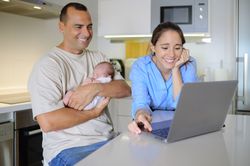 A man and woman holding a baby in front of a laptop