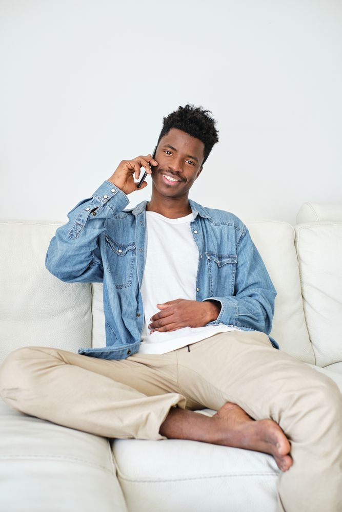 Content Black man talking on smartphone on sofa in house
