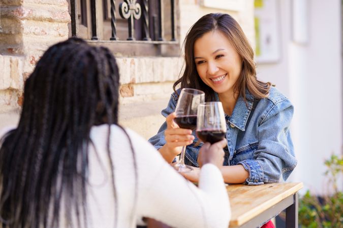 Female friends saying cheers with red wine at an outdoor table at a restaurant