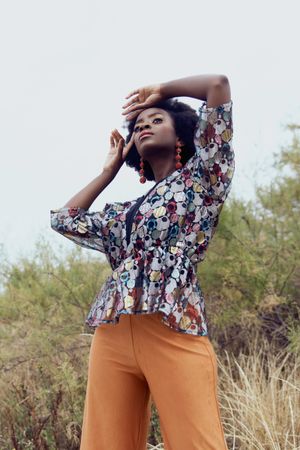 Black woman in colorful patterned top and brown pants standing