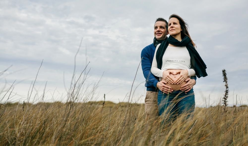 Pregnant woman making heart with hands on naked belly with partner