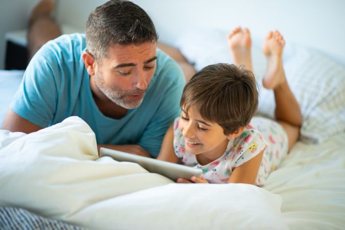Father with child playing on tablet in bed
