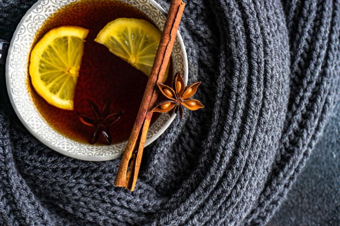 Top view of star anise and cinnamon balancing on tea cup surrounded by woolen knit
