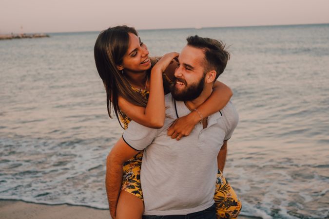 Amorous man carrying woman on arms along sandy beach