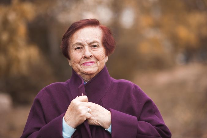 Portrait of older woman in purple coat standing near yellow trees