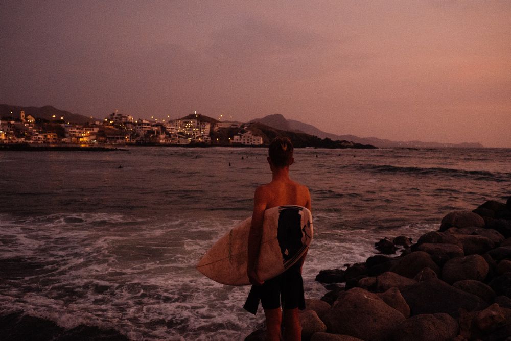 Back of male surfer holding board looking over at sunset view