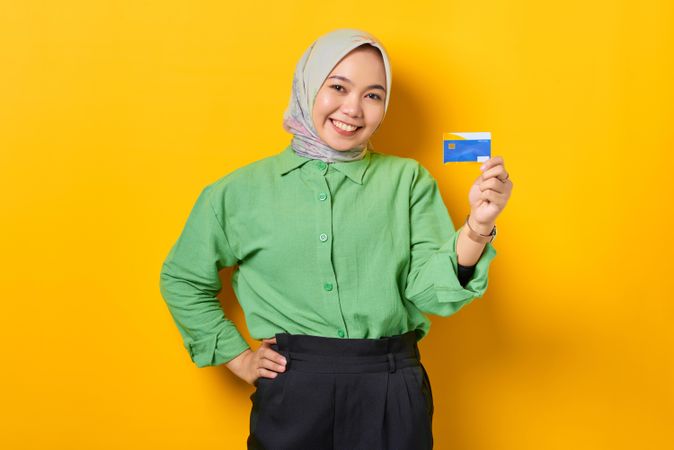 Smiling Muslim woman in headscarf and green blouse holding credit card