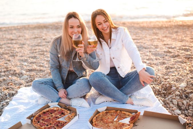 Two young women drinking wine and having a pizza at the beach