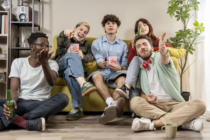 Group of multiracial young friends cheering and eating popcorn together during a home movie night