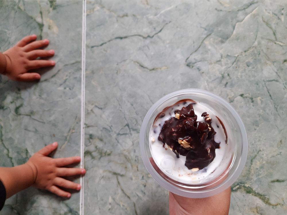 Vanilla Chocolate Ice Cream in Plastic Cup with Child’s Hands Reaching on Tiled Floor