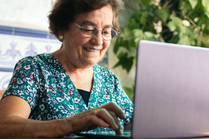 Mature woman with glasses using a laptop and a notebook at home