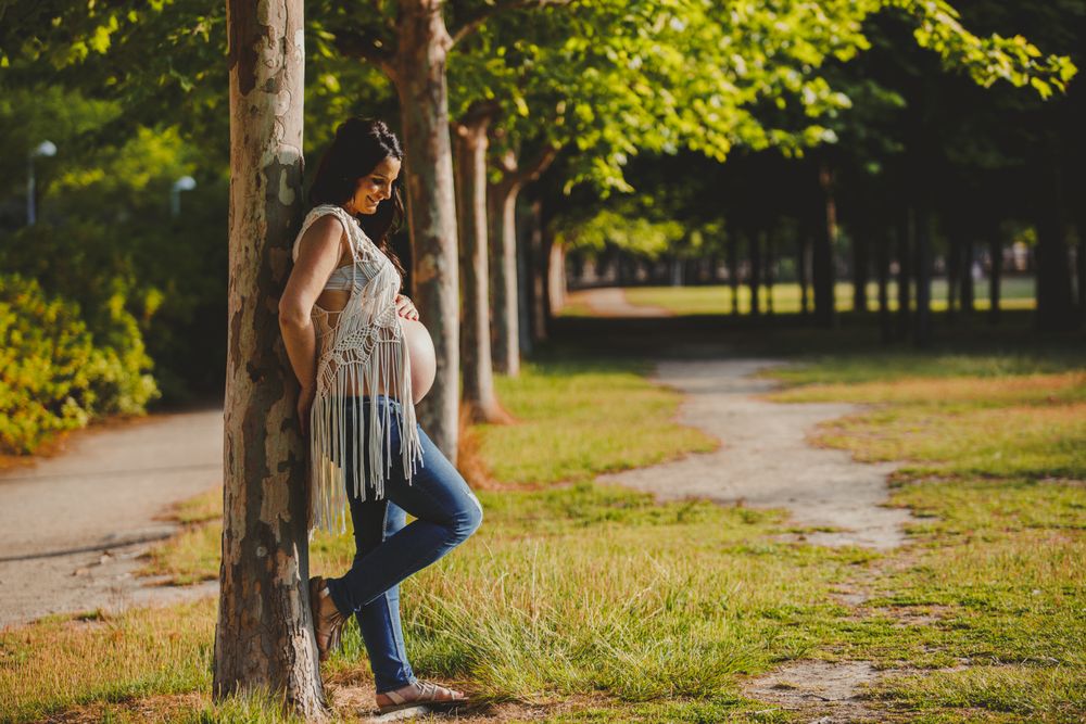 Pregnant female leaning on tree in park