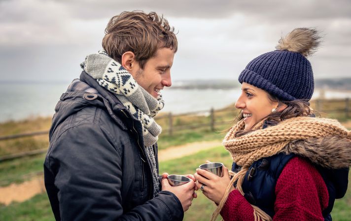 Man and woman facing each other and talking while holding warm beverage on cold day