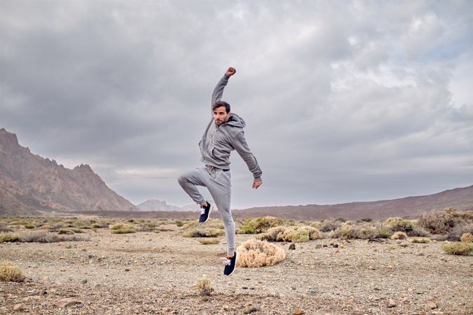Happy man jumping with raised hand in nature in highland