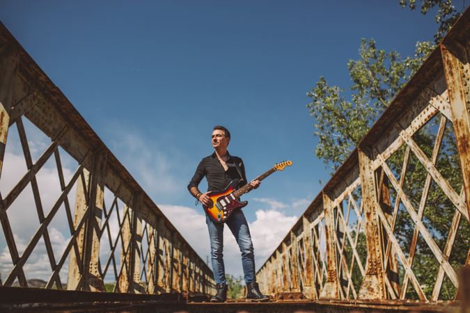 Man with guitar standing on bridge