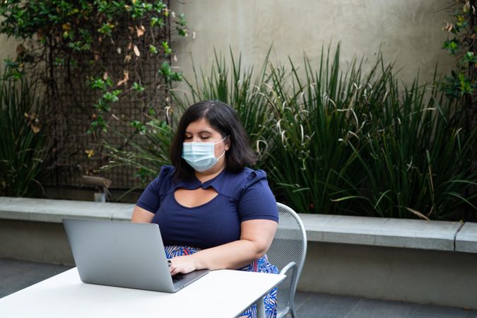 Woman in face mask working on laptop outside