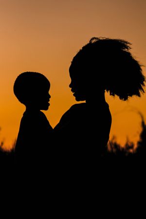 Silhouette of mother holding a baby standing outdoor at sunset