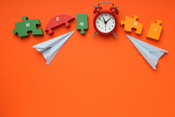 Puzzle pieces spelling “memory” on orange background with alarm clock, copy space
