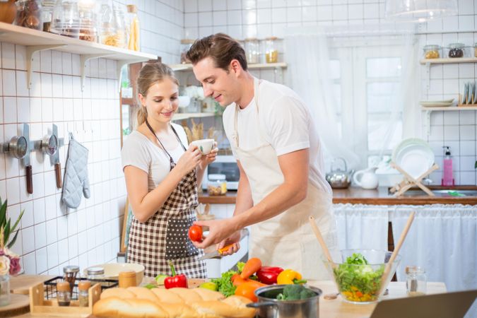 Man and woman preparing a salad at home with woman sipping tea