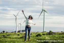 Happy woman in light sweater and denim pants standing beside wind turbines 437pj4