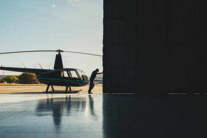 Mechanic pushing the door of a hangar with a helicopter