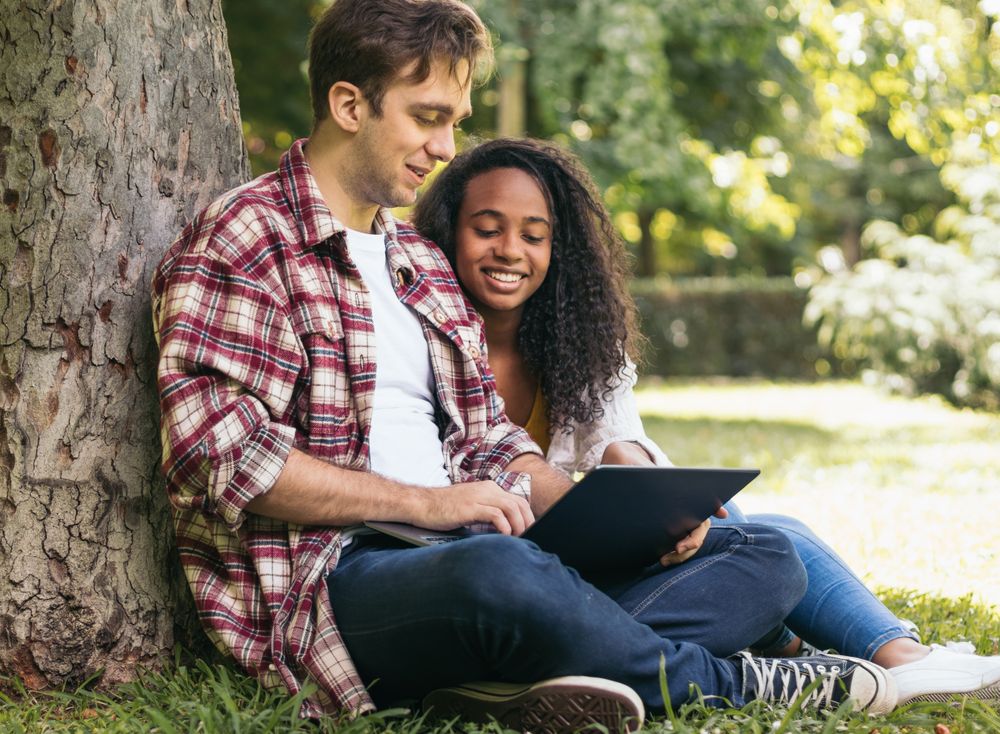 Multiracial couple studying in the park with laptop