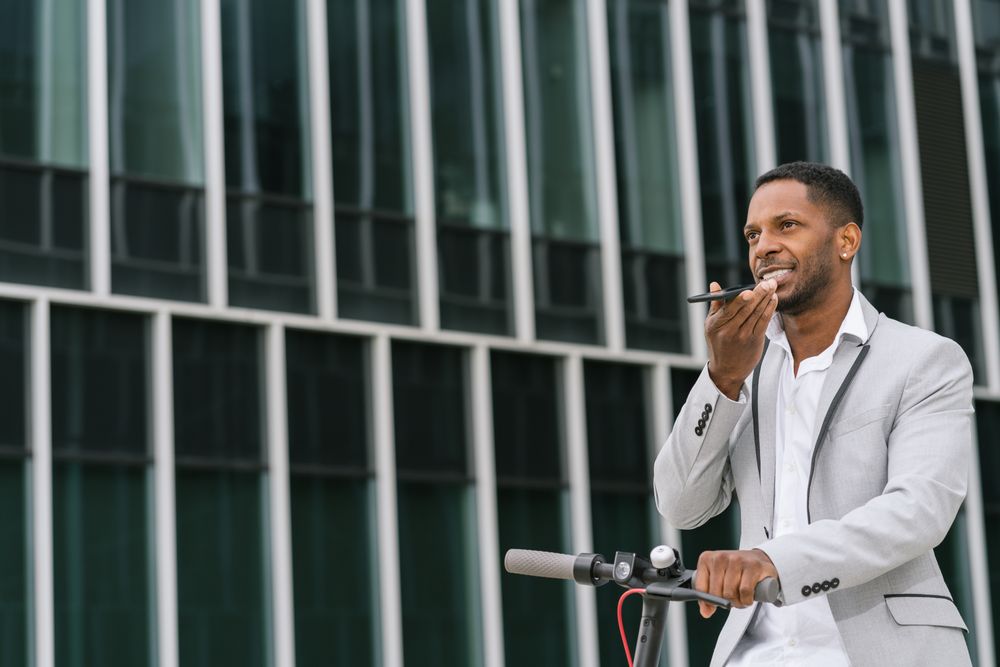 Smiling Black man riding scooter and speaking on smartphone