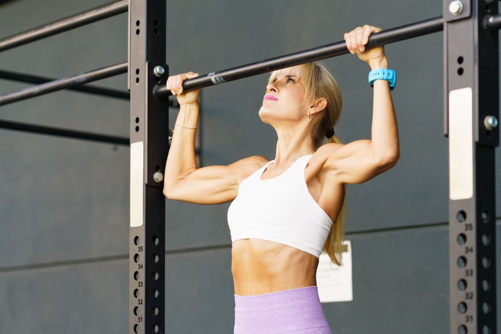 Strong woman hanging on bar in gym