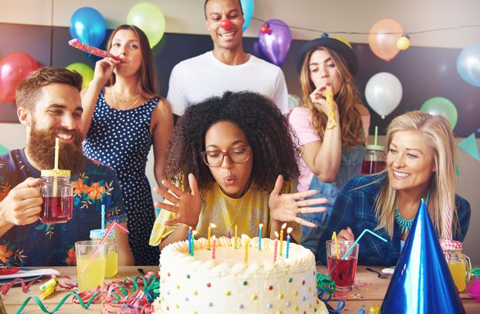 Black woman blowing out her birthday candles as friends behind her blow streamers