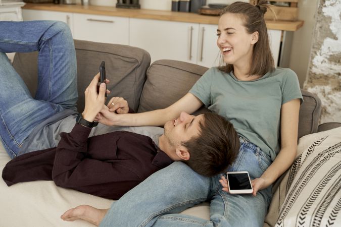 Chilling couple spending time together on sofa browsing smartphone