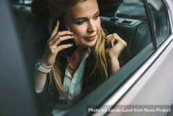 Young businesswoman talking on the cellphone while sitting in back seat of a car 4d72N5