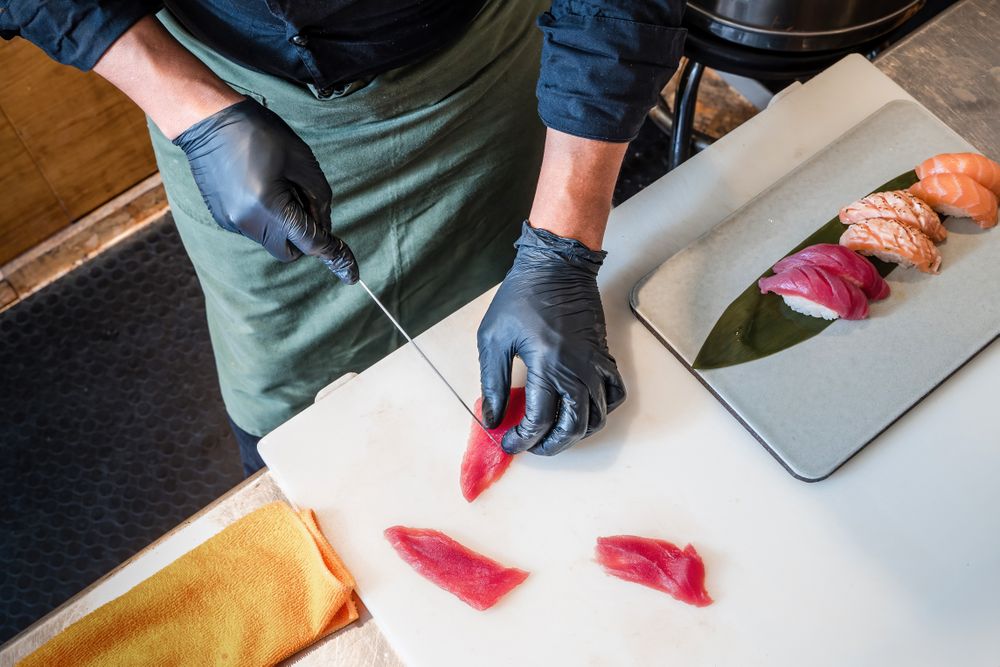 Chef preparing sushi slicing fresh tuna fish in restaurant kitchen