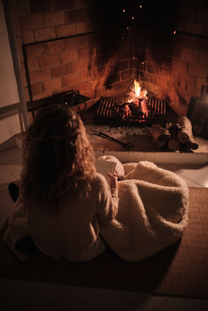 Unrecognizable woman covered with blanket sitting near fireplace