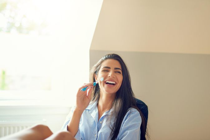 Woman smiling using toothbrush in bright room