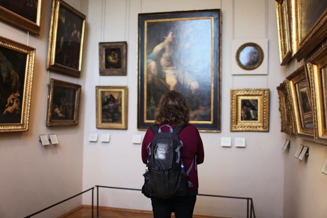 Back view of a person with backpack looking at a painting in a museum