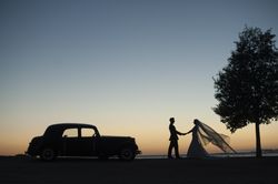 Woman and man holding hands near vintage car at sunset