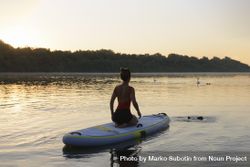 Woman sitting on paddleboard looking at two swans in lake bEvLN0