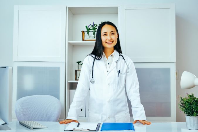 Confident Asian doctor at clinic standing behind her desk
