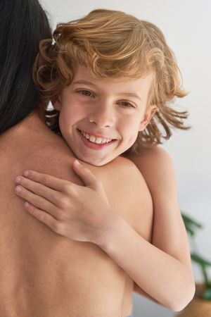 Delighted kid embracing anonymous topless mom