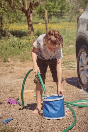 Little boy pouring water in bucket in countryside