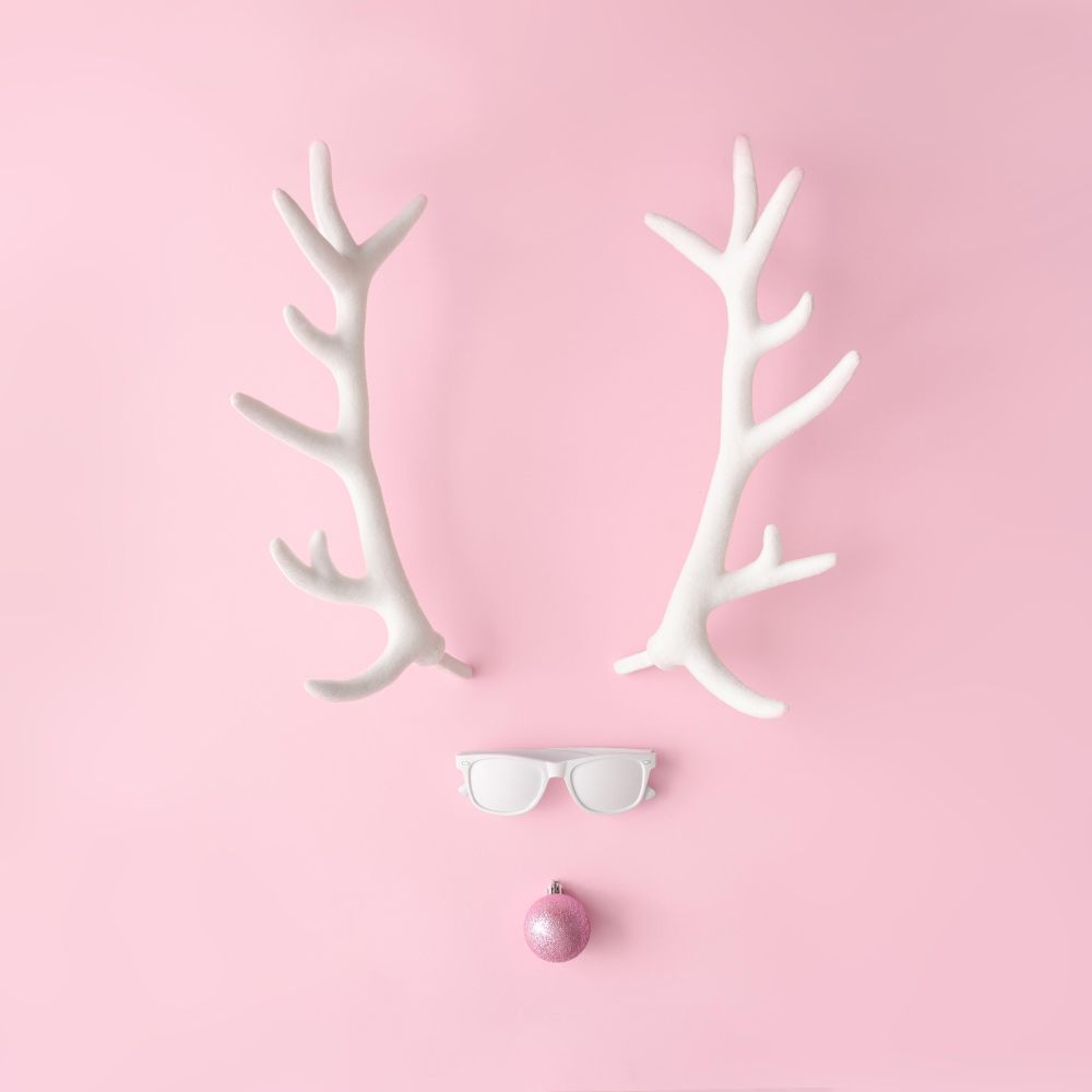 Reindeer face made of sunglasses and pink bauble on pink background