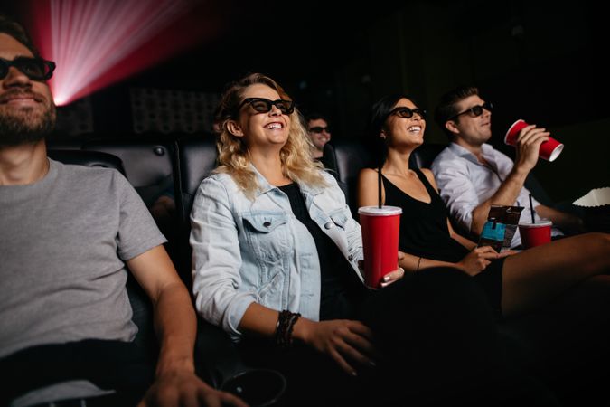 Young women and men watching 3d movie in cinema laughing