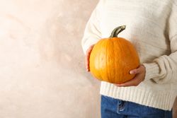 Young woman holding pumpkin on brown background, copy space