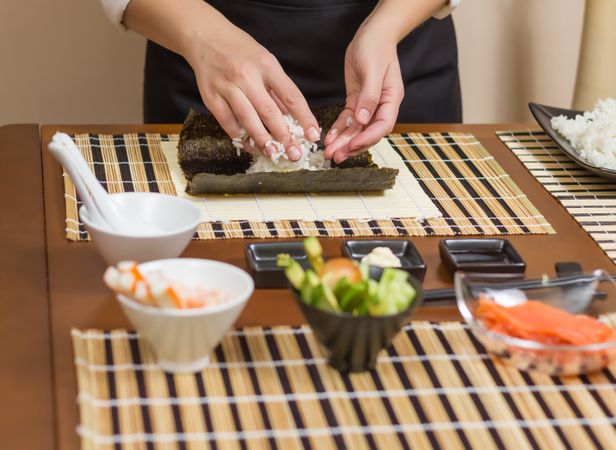 Hands of woman chef filling Japanese sushi rolls with rice on a nori seaweed sheet